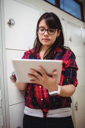 Female student using digital tablet in locker room at collegeの写真素材