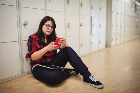 Female student using mobile phone in in locker room at collegeの写真素材