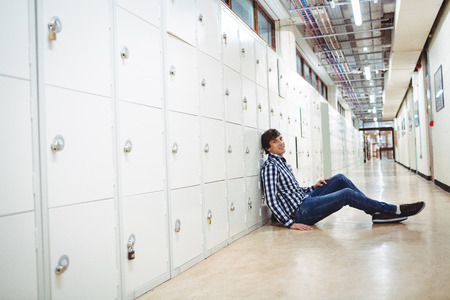 Portrait of smiling student sitting in locker room at collegeの写真素材