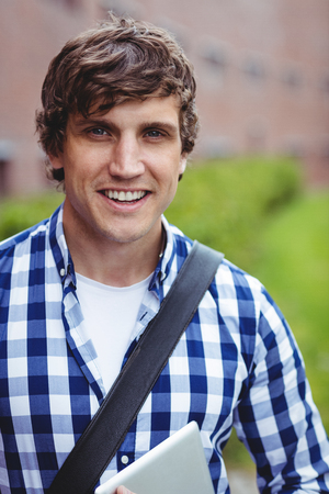 Portrait of smiling student standing in college campus with digital tabletの写真素材