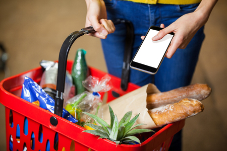 Mid section of woman holding groceries and mobile phone in supermarketの写真素材