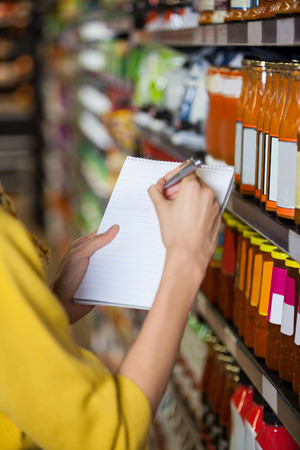 Mid section of woman at grocery section writing in notepad at supermarketの写真素材