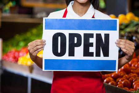 Mid section of female staff holding open signboard in organic section of supermarket