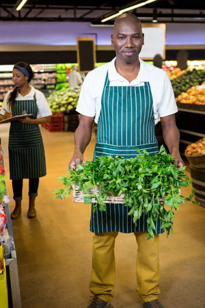 Portrait of smiling male staff holding a basket of fresh vegetables at supermarketの写真素材