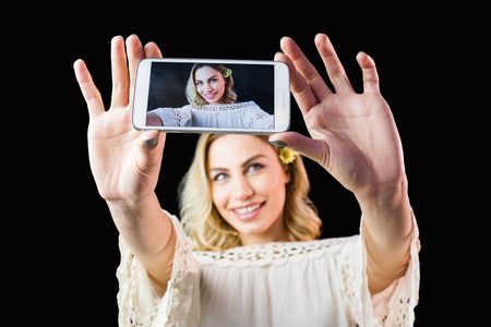 Beautiful woman clicking photo from mobile phone against black backgroundの写真素材