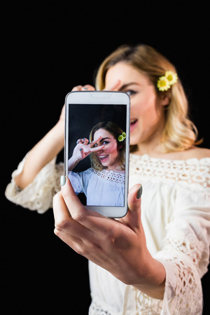 Portrait of beautiful woman clicking photo from mobile phone against black backgroundの写真素材