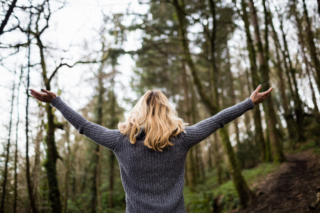 Rear view of woman standing with arms outstretched in forestの写真素材
