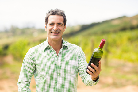 Portrait of smiling vintner holding bottle of wine in vineyardの写真素材