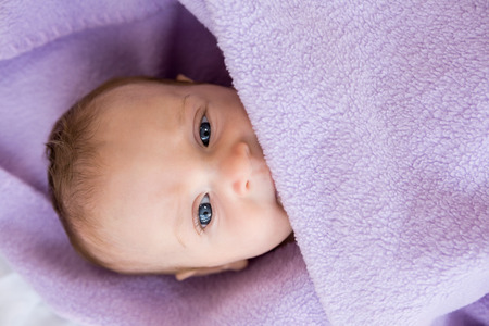 Baby boy relaxing on bed with blanket at homeの写真素材