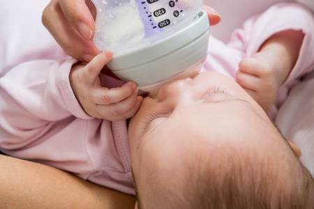 Mother feeding baby with milk bottle in living room at home
