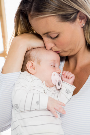 Mother holding and kissing her baby boy at homeの写真素材
