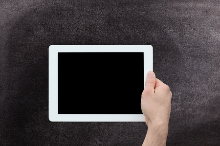 Digital composite of Hand holding tablet computer with chalkboard background