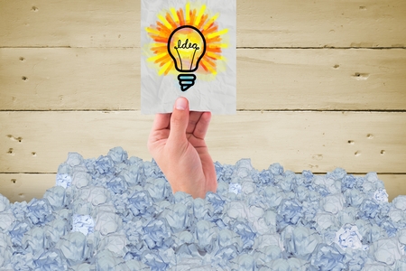 composite of hand holding idea lightbulb with crumpled papers and wood backgroundの写真素材