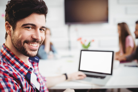 Portrait of confident young male executive with laptop in meeting room at creative officeの写真素材