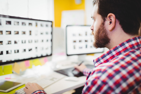 Close-up of young male editor concentrating on photographs in computer at creative office