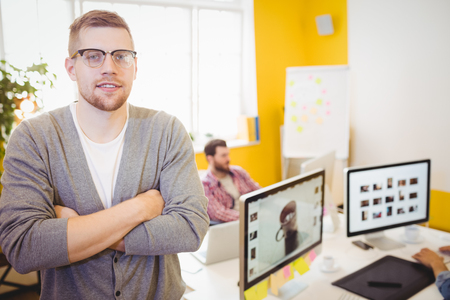 Portrait of confident young male editor with arms crossed at creative officeの写真素材