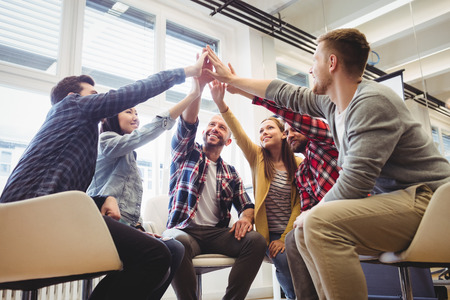Low angle view of happy creative business people giving high-five in meeting room at creative office