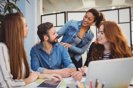 Businessman with happy female coworkers at desk in creative officeの写真素材