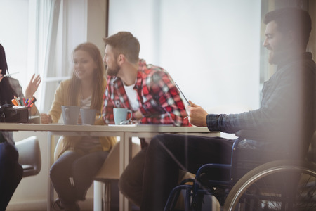 Businessman on wheelchair using digital tablet against photo editors in meeting room at creative officeの写真素材