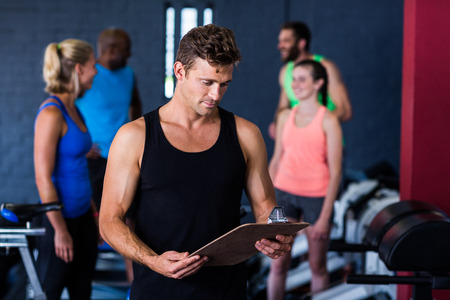Gym trainer with clipboard while people standing in backgroundの写真素材