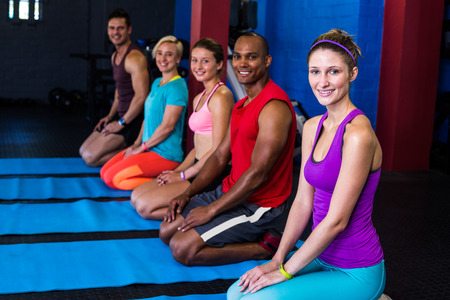 Portrait of smiling people exercising while kneeling in gymの写真素材