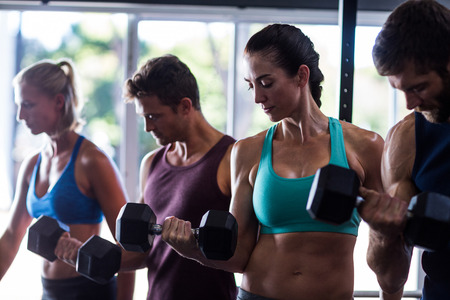 Young friends holding dumbbells while working out in gymの写真素材