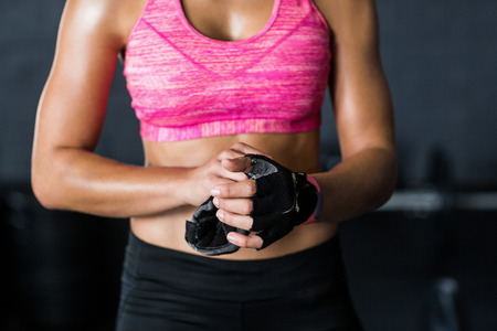 Midsection of female athlete removing gloves while standing in gymの写真素材