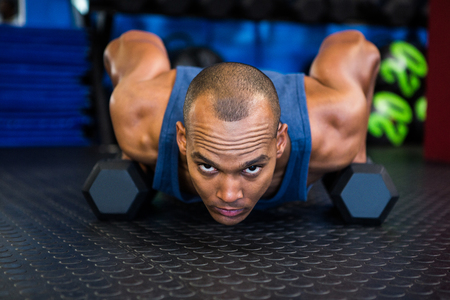 Portrait of serious man doing push-ups with dumbbell in gymの写真素材