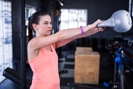 Female athlete holding kettlebell while standing in gymの写真素材