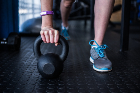 Low section of female athlete holding kettlebell while exercising in gymの写真素材