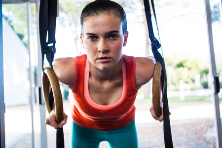 Portrait of confident athlete holding gymnastic rings in gym