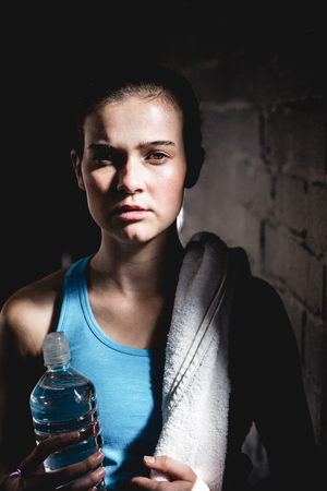 Portrait of serious female athlete holding water bottle in gymの写真素材