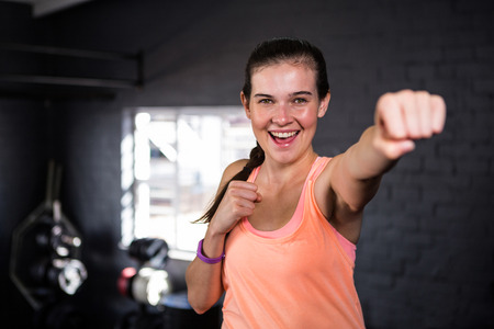 Portrait of smiling young woman punching while standing in gym