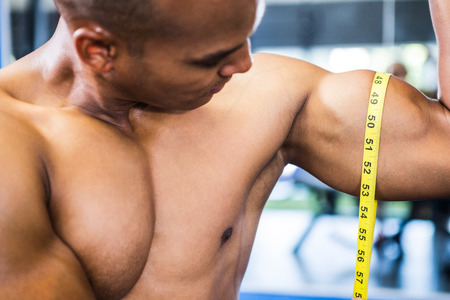 Close-up of muscular man measuring biceps with tape measure in gymの写真素材