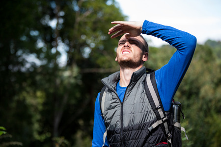 Male hiker shielding his eyes in forest