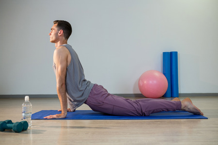 Man doing cobra pose on exercise mat in gymの写真素材