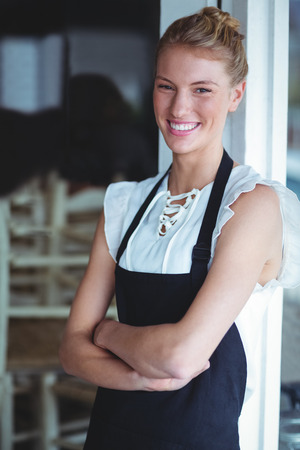 Portrait of smiling waitress standing with arms crossed outside the cafeの写真素材