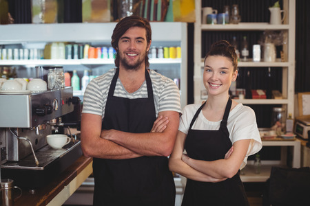 Portrait of waiter and waitress standing with arms crossed in cafeの写真素材
