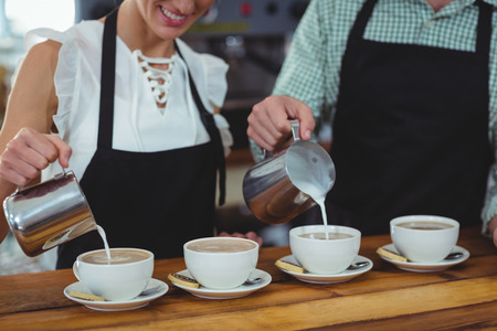 Mid section of waiter and waitress making cup of coffee at counter in cafeの写真素材