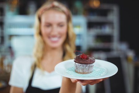 Waitress holding a plate of cupcake in caféの写真素材