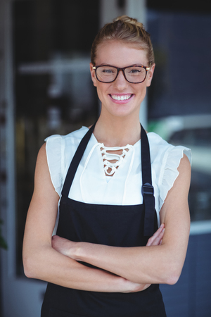 Portrait of smiling waitress standing with arms crossed outside the cafeの写真素材