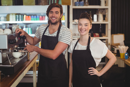 Portrait of waiter and waitress making cup of coffee at counter in cafeの写真素材
