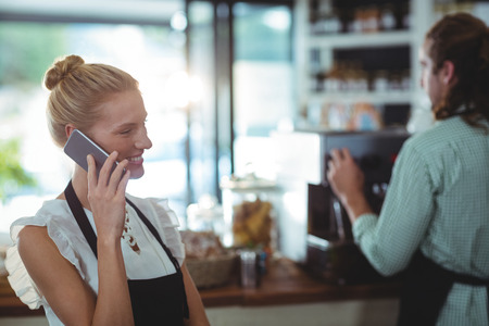 Smiling waitress talking on mobile phone in cafeの写真素材