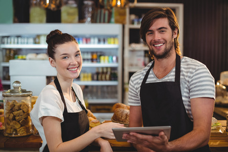 Smiling waiter and waitress using digital tablet at counter in cafeの写真素材