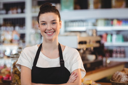 Portrait of smiling waitress standing with arms crossed in cafeの写真素材