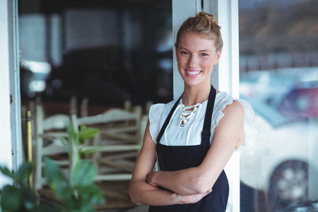 Portrait of smiling waitress standing with arms crossed outside the cafe