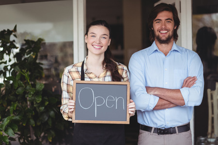 Man and waitress holding chalkboard with open sign outside the cafe