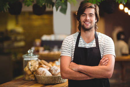 Portrait of smiling waiter standing with arm crossed in cafe