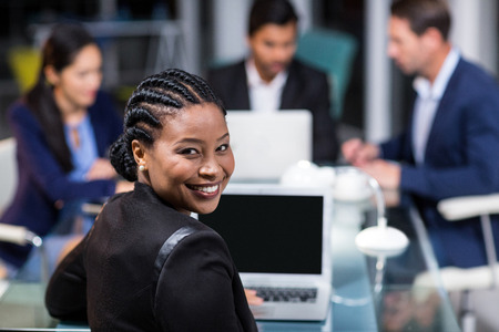Portrait of businesswoman smiling at camera while colleagues interacting in the backgroundの写真素材