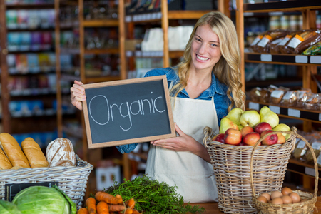 Portrait of smiling staff holding organic sign board in organic section of super marketの写真素材
